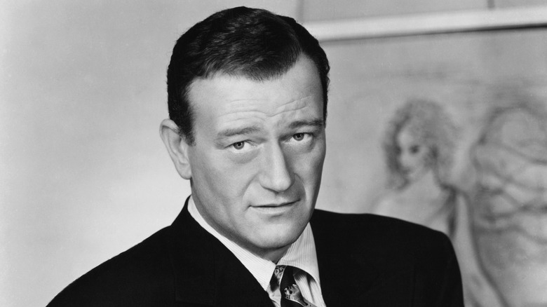 A black and white photograph of the late actor John Wayne in a tuxedo staring at the camera.