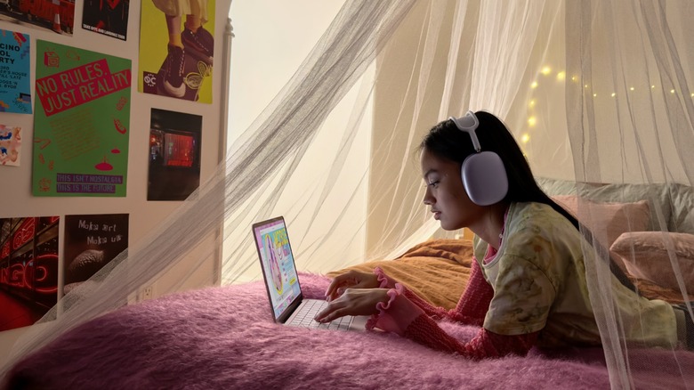 Woman in bedroom listening to music on MacBook Neo while typing on keyboard