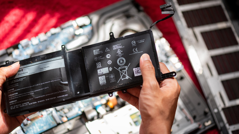 Someone holding and removing a laptop battery from its shell