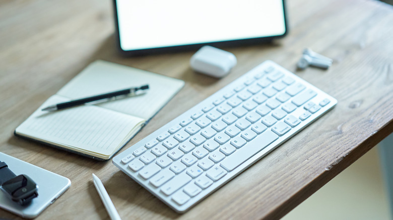 Image of a keyboard, headphones, tablet, and journal on a wooden desk.