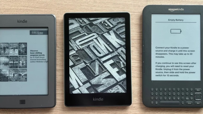 Kindle Touch (2011), Kindle Paperwhite 11, and Kindle Keyboard side-by-side on a wooden table