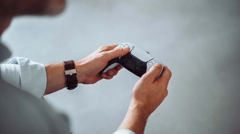 a person holding a PlayStation 5 controller in their hands while sitting