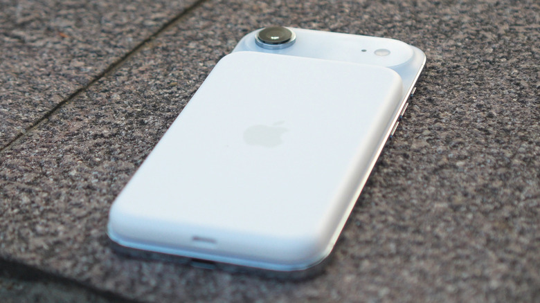 An iPhone Air with its complementary Battery Pack lying on a concrete surface.