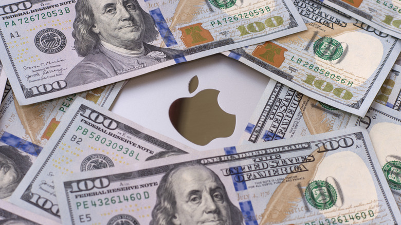 The Apple logo on a silver MacBook is surrounded by crisp $100 bills