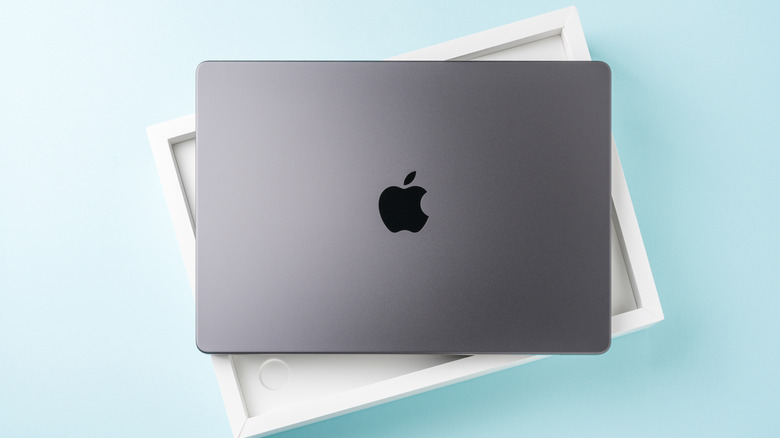 A silver MacBook sits on top of its box against a light blue backdrop