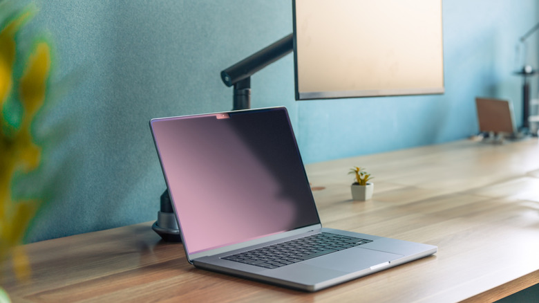 Close up of a laptop on a desk connected to a monitor on an adjustable arm.