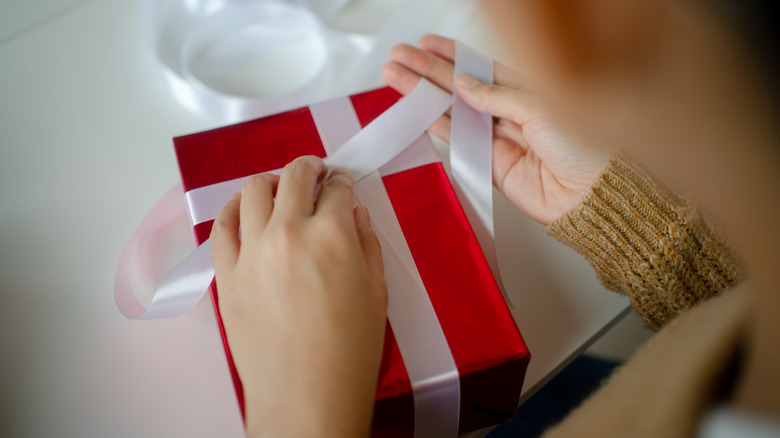 A woman tying a ribbon around a gift.