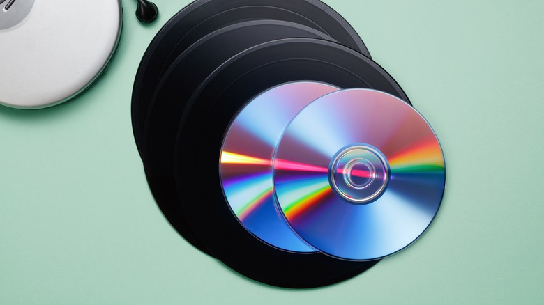 Vinyl records and CDs piled up on a table next to a CD player