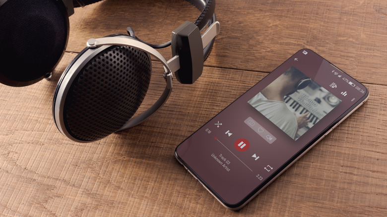 A pair of headphones sitting on a wooden table next to a phone playing music