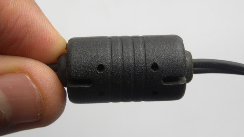 A finger and thumb holding a black ferrite bead against a white backdrop