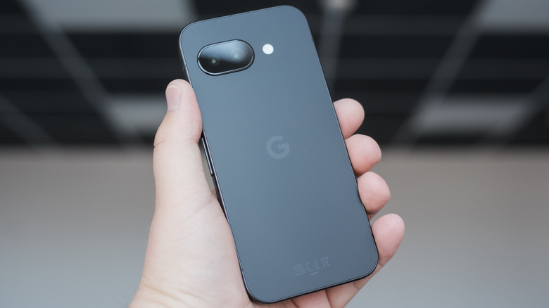 A closeup of a black Google Pixel 9a as its being held face down in an individual's left hand