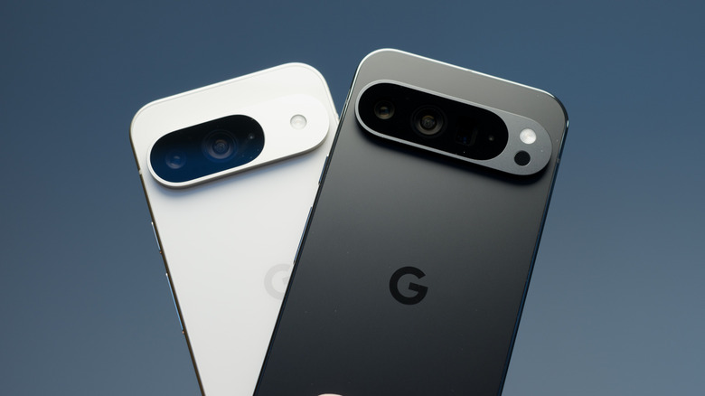 A white Google Pixel 9 Pro standing slightly crooked behind a black Google Pixel 9 Pro XL that is also slightly crooked