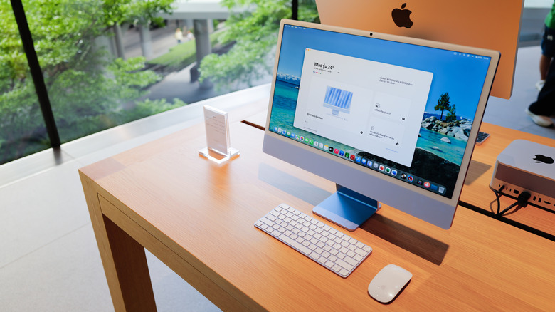 Apple iMac desktop computer setup with a keyboard and mouse on a wooden display table inside an official retail store