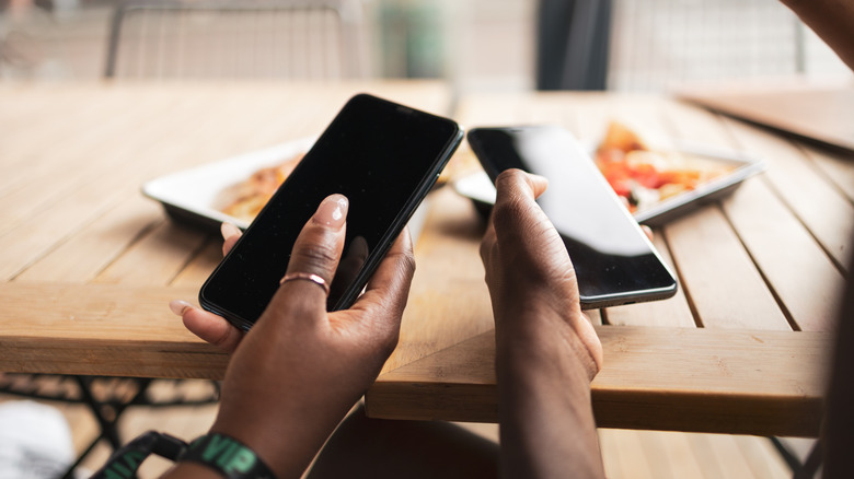 Two hands holding two mobile devices together in close proximity at a restaurant
