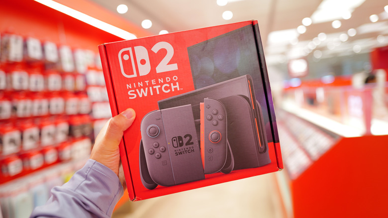 Person holding a Switch 2 box in a gaming store, blurred background