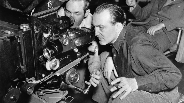 Fritz Lang peers through a film lens with his infamous monocle alongside a team of crew memebrs.