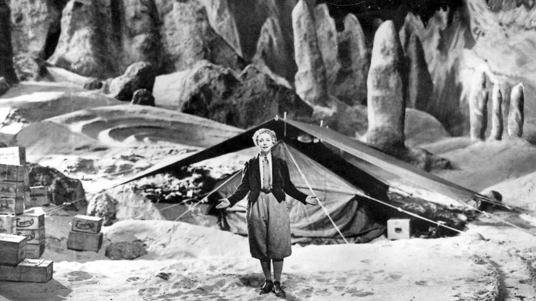 A woman stands with her palms up in front of a tenat before a rugged lunar backdrop.