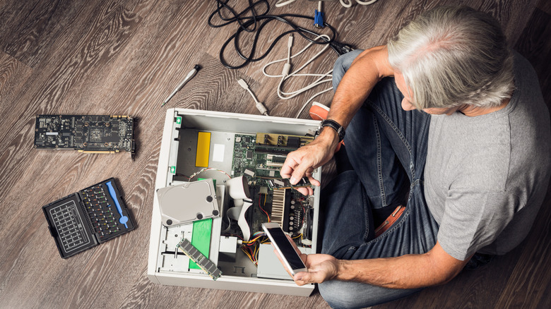 Man repairing desktop computer on floor with tools and internal PC components nearby