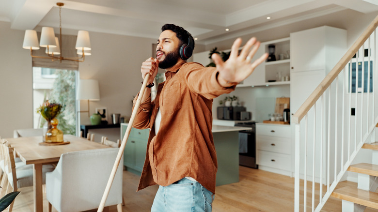 a man listens to music on through his headphones while dancing and using a broom as a mic