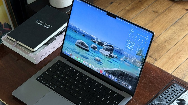 Apple's MacBook Pro on a table with some remotes and books around it