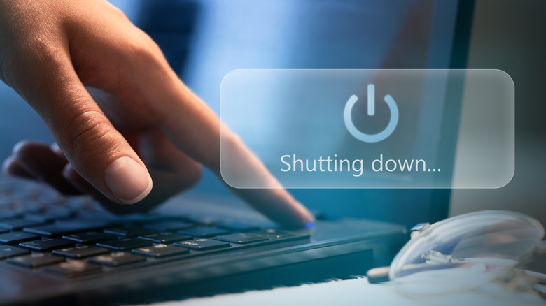 Person pressing the power button on a laptop with the logo and shutting-down message visible.