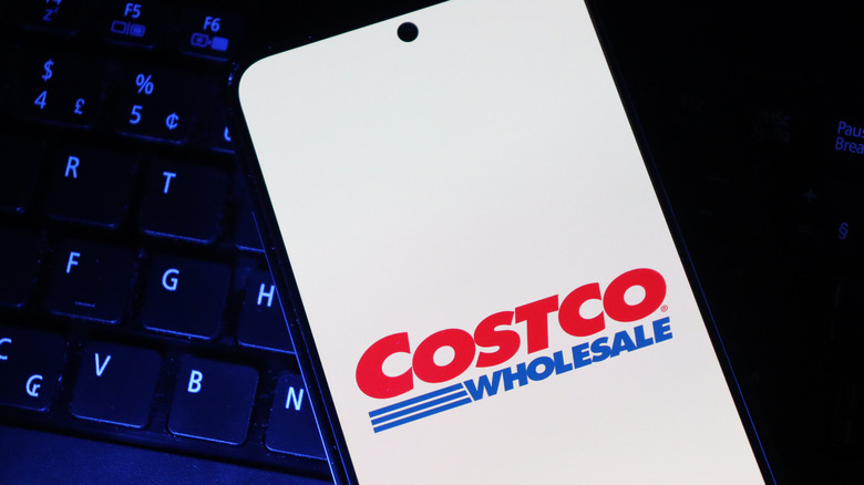 A phone with a costco logo on the screen, sitting on a laptop's keyboard in the dark