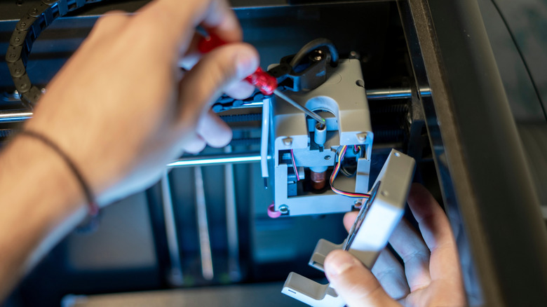 Close-up of hands working on internal components of 3D printer