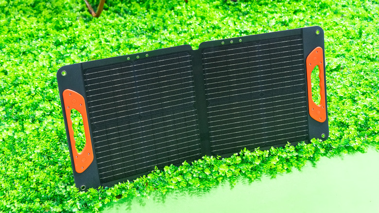 A foldable solar panel with orange handles standing on bright green grass.