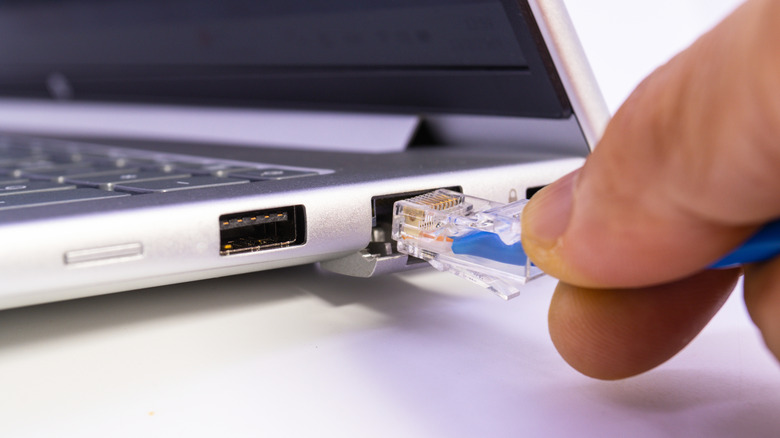 A person connecting a blue LAN cable into an Ethernet port on a laptop