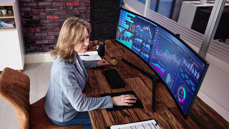 A woman works at an ultrawide curved monitor that takes up a lot of desk space