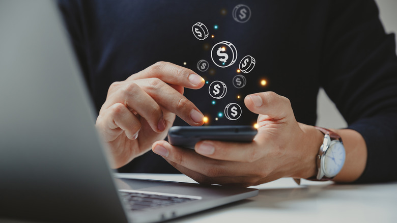 Dollar coin graphics floating away from a smartphone in someone's hands