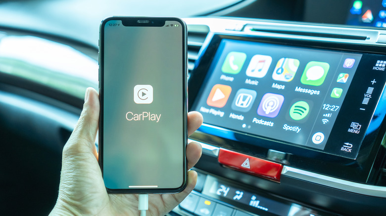 A hand holding an iPhone being charged in the car, with CarPlay loading