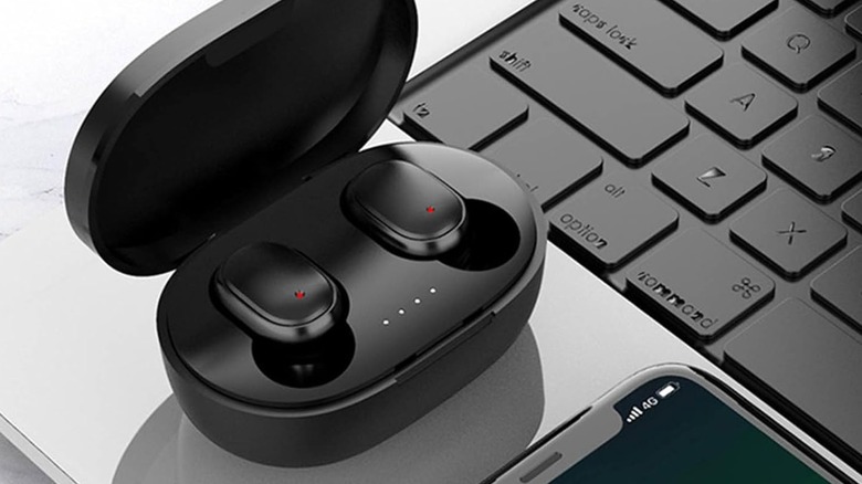 Generic cheap black Bluetooth earbuds in charging case on laptop next to smartphone