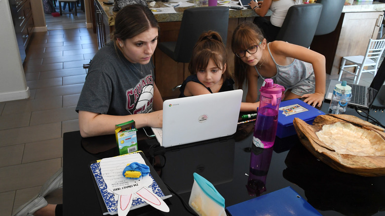 A teenager looking at a Chromebook next to two children