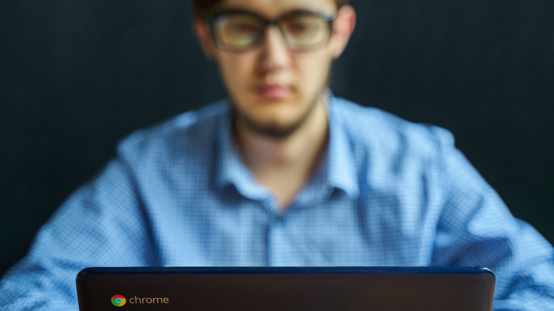 A young man faded out in the background using a Chromebook.