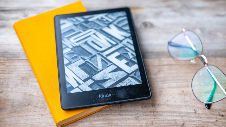 kindle e-reader on top of a yellow book on a wooden table