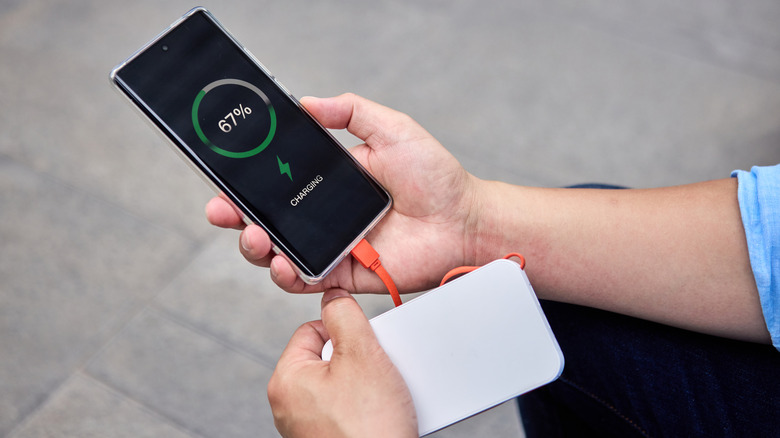 Person charging a smartphone with a portable power bank, showing 67% battery on screen