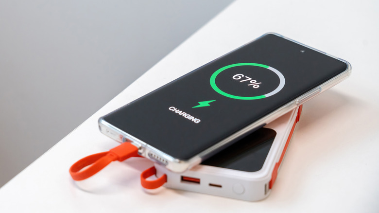 Smartphone charging on top of a portable power bank, showing 67% battery on screen
