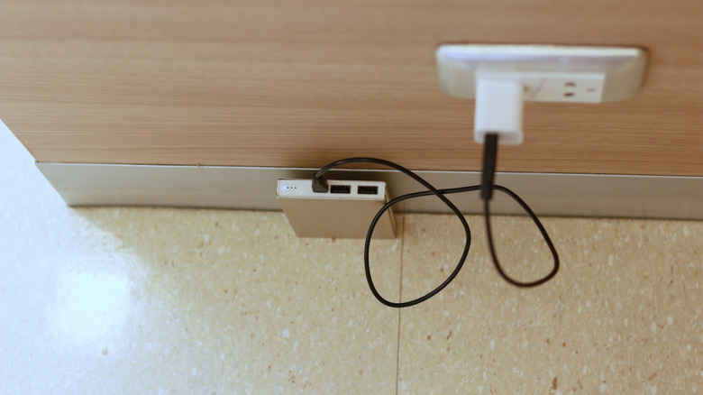 A power bank placed on the floor while connected to a wall socket above it for charging