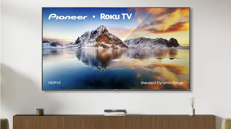 A Pioneer Roku TV mounted on a white wall with furniture under it.