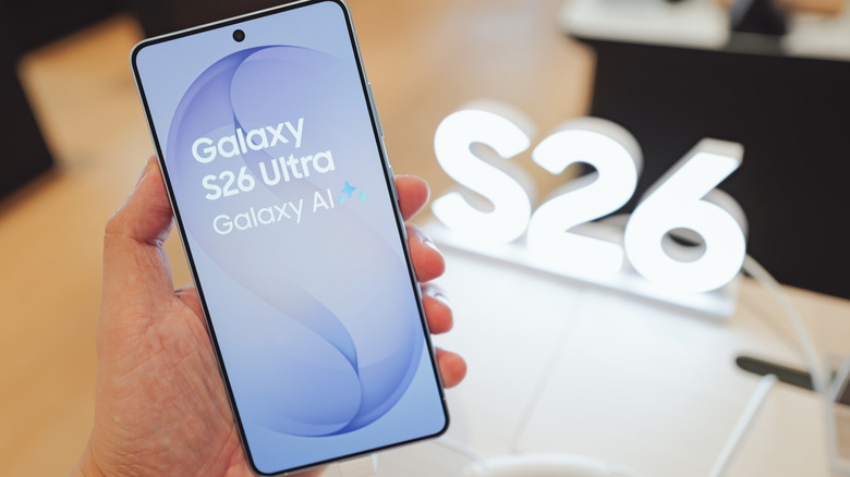 A Samsung Galaxy S26 Ultra phone being held in a hand with a light shaped like the words S26 in the background