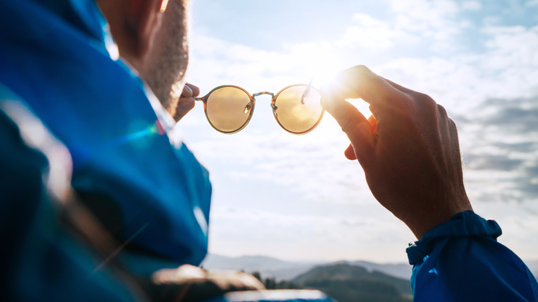 A hiker holding a pair of polarized sunglasses outdoors