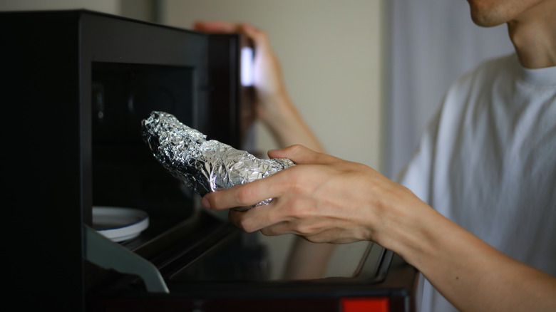 A person placing food wrapped in aluminum foil inside a microwave