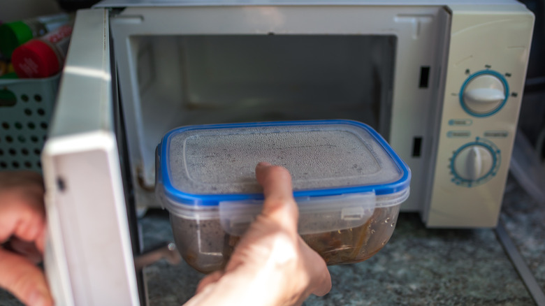 A person putting food in a plastic container into a microwave