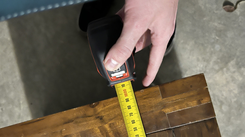 A close-up of someone measuring a wooden surface with a tape measure