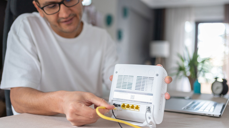 A man connecting an Ethernet cable to a router