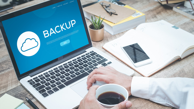 person using laptop with cup of coffee, screen displays blue image with backup written in large letters.