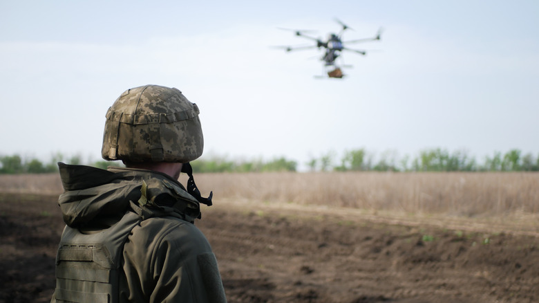 A soldier staring at a drone in the distance in an open field