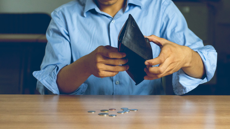 a man holding an empty wallet with some change on the table