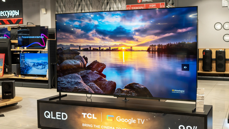 A QLED word graphic that a person is pointing a remote toward.